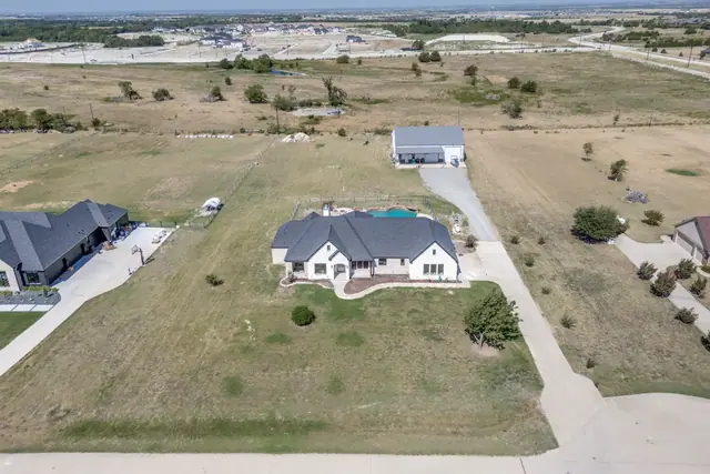 Aerial view from the street showing the front elevation of the home across its lawn, with the pool behind it and the workshop/barn at the far end of the property