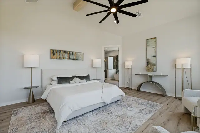 Primary bedroom with a large bed, side tables, and a rug on wood floors