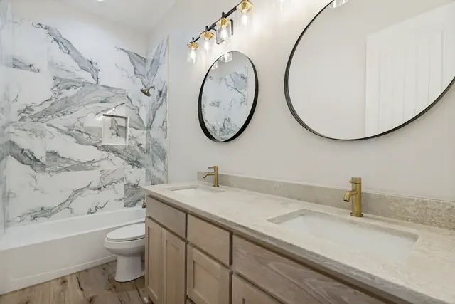 Bathroom with a marble accent wall, round mirrors, and a double vanity