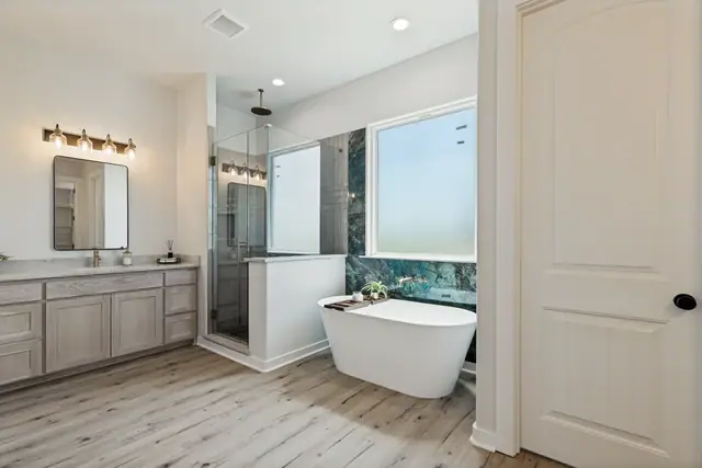 Primary bathroom with a freestanding tub against a marble wall, glass shower, and vanity