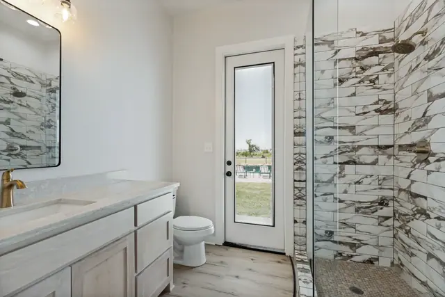 Bathroom with a marble-tiled shower, vanity, and a glass door opening to the pool deck