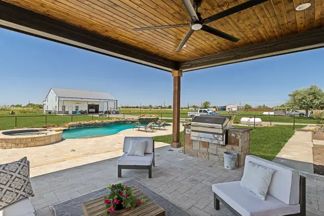 View from the covered patio past the built-in grill to the pool and spa