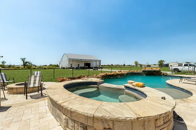 Raised spa and pool with stone coping, with the workshop/barn beyond the fence