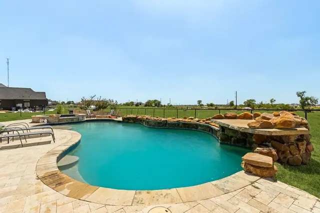 Freeform pool with blue water, stone decking, and a rock water feature
