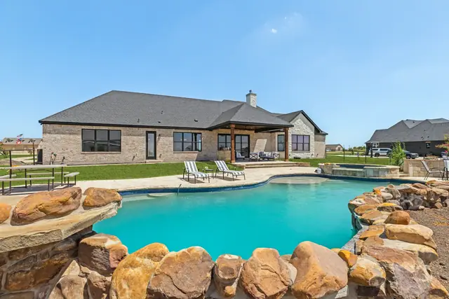 Rear view of the house across the pool, showing the covered patio and stone decking