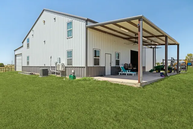 Metal-clad workshop/barn with a large covered apron, open bay, and equipment beside it